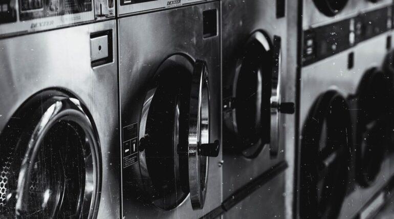 Row of vintage stainless steel commercial washing machines in a laundromat in black and white